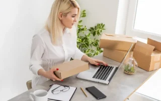 Antreprenoare pregatind colete si gestionand comenzi pe laptop pentru lansarea unui magazin online