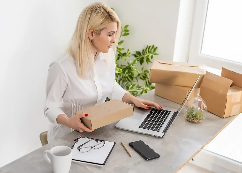 Antreprenoare pregatind colete si gestionand comenzi pe laptop pentru lansarea unui magazin online