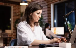 O antreprenoare concentrată lucrând pe laptop într-un birou modern, monitorizând performanța tehnică a site-ului pentru o experiență de utilizare superioară.