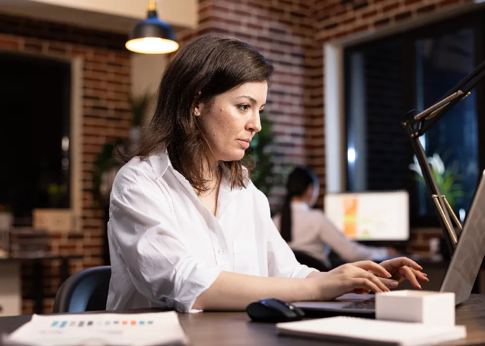 O antreprenoare concentrată lucrând pe laptop într-un birou modern, monitorizând performanța tehnică a site-ului pentru o experiență de utilizare superioară.