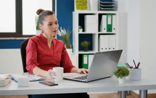 Manager de eCommerce lucrează la laptop în birou, cu o cană de cafea pe birou, planificând un magazin online.