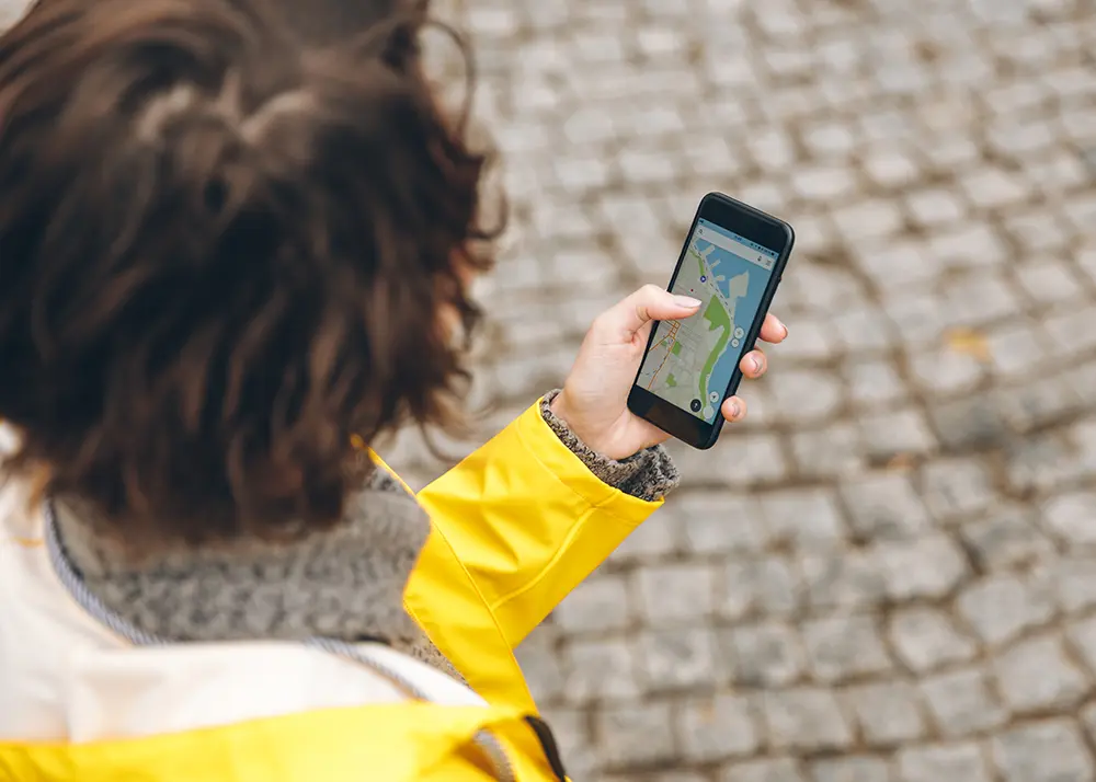 Persoană care caută o afacere locală pe Google Maps de pe telefon, pe o stradă pavată