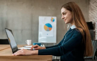 Femeie de afaceri care analizează date pe laptop într-un birou modern, cu grafice de performanță în fundal