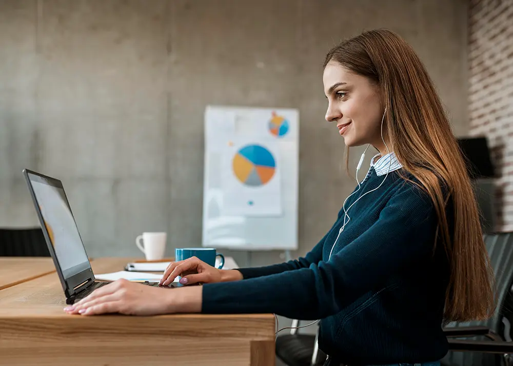 Femeie de afaceri care analizează date pe laptop într-un birou modern, cu grafice de performanță în fundal