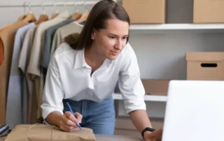 Persoană lucrând la laptop cu documente și materiale de studiu, ilustrând analiza și implementarea sistemelor de plată pentru magazine online românești