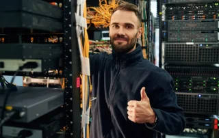 Specialist IT zâmbind și aprobând cu degetul mare ridicat într-un centru de date modern, ilustrând fiabilitatea unui hosting WordPress de calitate
