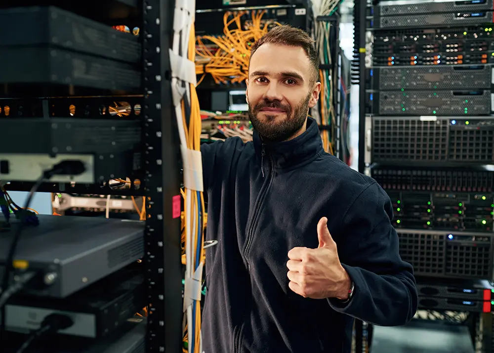 Specialist IT zâmbind și aprobând cu degetul mare ridicat într-un centru de date modern, ilustrând fiabilitatea unui hosting WordPress de calitate