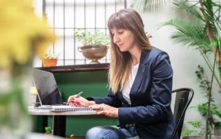 Antreprenoare concentrată analizând pe laptop și notițe scrise de mână opțiunile dintre WooCommerce și Shopify pentru magazinul ei online din România