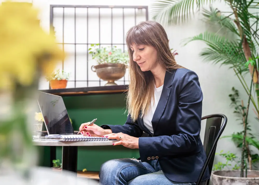 Antreprenoare concentrată analizând pe laptop și notițe scrise de mână opțiunile dintre WooCommerce și Shopify pentru magazinul ei online din România